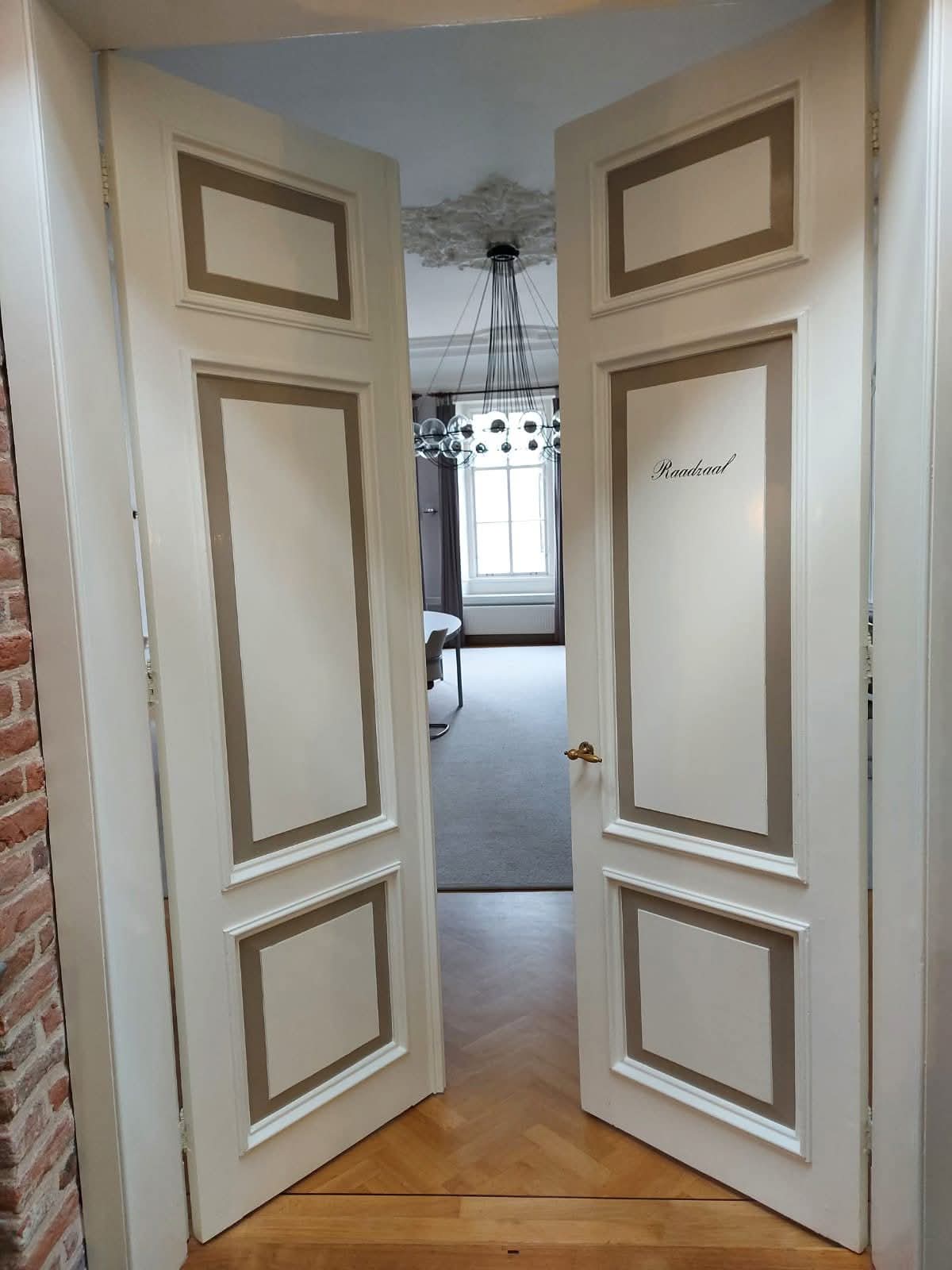 Twee witte deuren die leiden naar de raadzaal van Hattem staan open op een kier. Door deze kier zie je een raam, een kandelaar en een stukje van een vergadertafel.